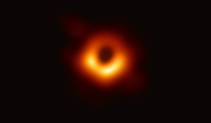 Foto do buraco negro no centro da galáxia M87. A imagem mostra um anel laranja incandescente desfocado formado quando a luz se curva na gravidade em torno do buraco negro que é 6,5 bilhões de vezes mais massivo que o Sol.