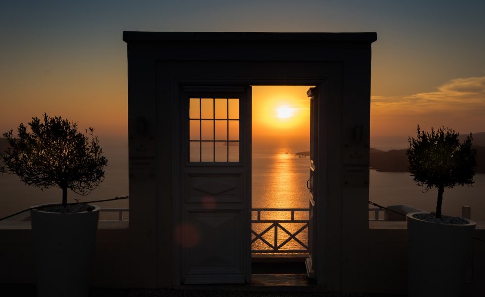 Se observa o Sol no horizonte entrando por uma porta e uma janela abertas nas margens de águas calmas. Do lado esquerdo e direito há duas árvores pequenas.