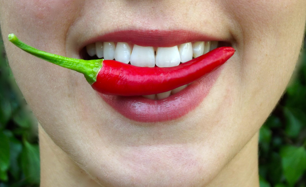 A imagem mostra uma boca com batom vermelho mordendo uma pimenta vermelha.
