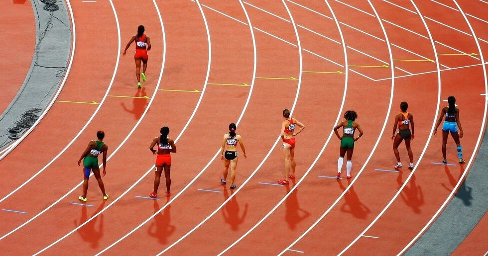 Oito corredoras, cada uma em uma raia olímpica. Sete delas nas marcas de largada e uma mais a frente, já correndo.
