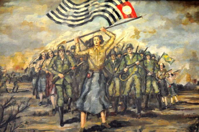 Pintura com mulher carregando bandeira do estado de São Paulo e soldados, homens e mulheres, atrás dela, uniformizados e carregando armas. Representação da Revolução Constitucionalista de 1934.