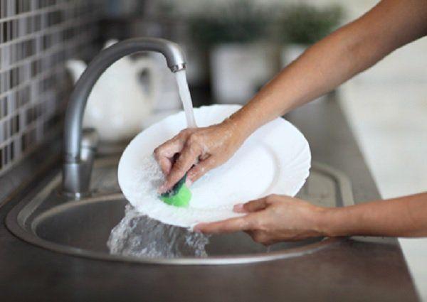 Pessoa lavando um prato com água corrente. 