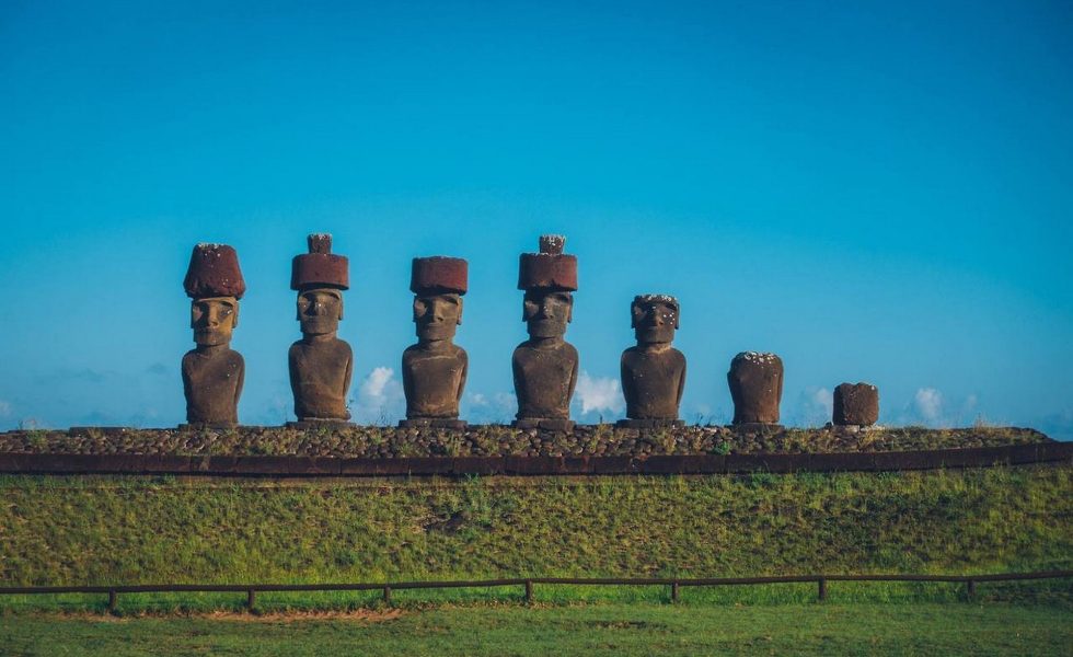 A foto é da escultura chamada Ahu Nau Nau, na praia de Anakena, na ilha de Páscoa. Na escultura há uma plataforma com sete estátuas em formato humanoides, chamadas moai, em estado de preservação variado, algumas com coroas de pedra. 