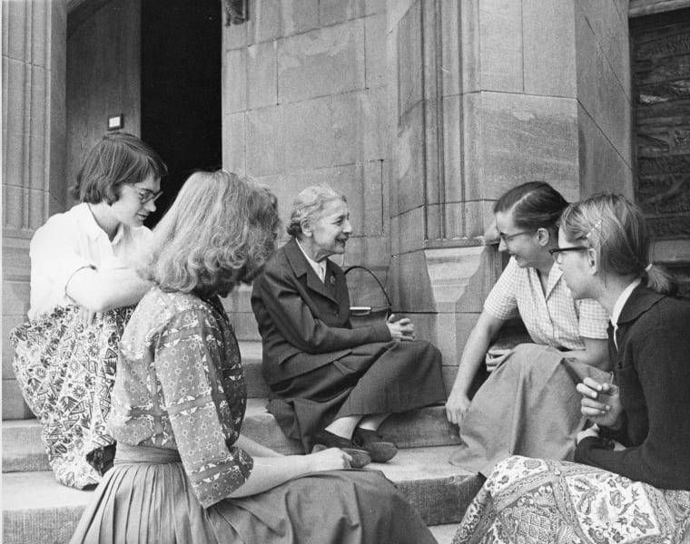 Fotografia em preto e branco, onde no centro dela se encontra a física Lise Meitner rodeada por duas estudantes ao seu lado direito e duas ao seu lado esquerdo, na Bryn Mawr College, Pensilvânia.
