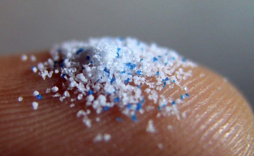 Imagem de diversas partículas de plástico, em escala micrométrica, sobre a região da digital de um dedo de uma pessoa.