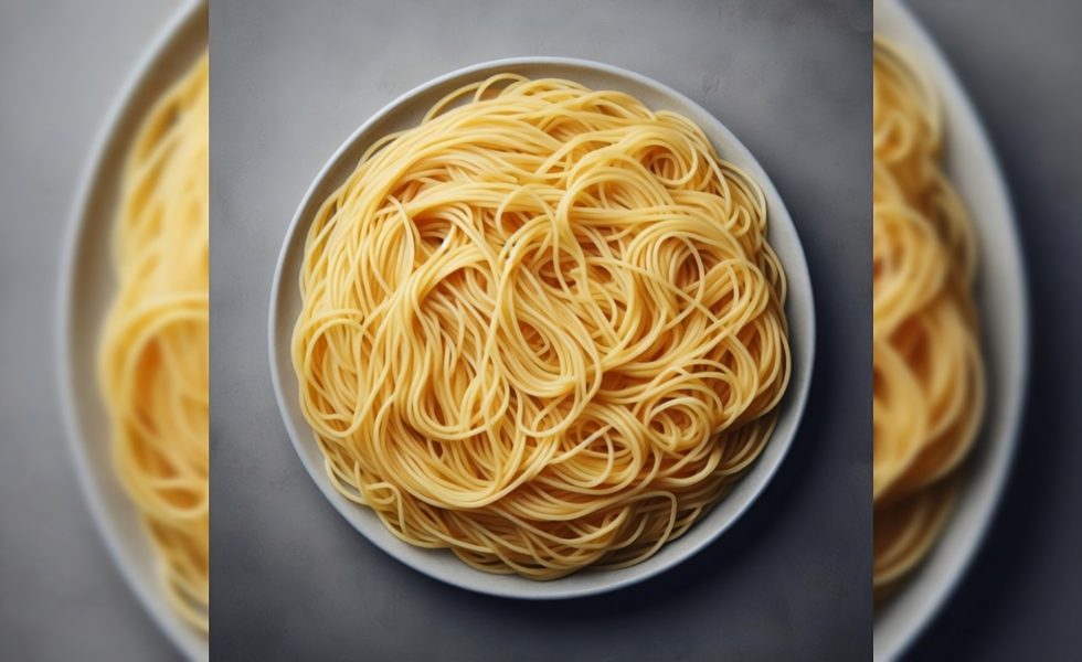 Imagem apresenta um prato branco sob uma superfície cinza, o prato está cheio de macarrão do tipo espaguete.